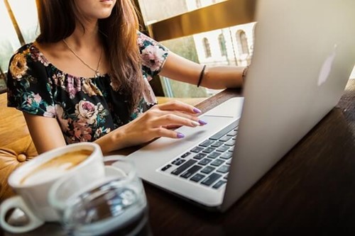 woman typing on a laptop next to a coffee